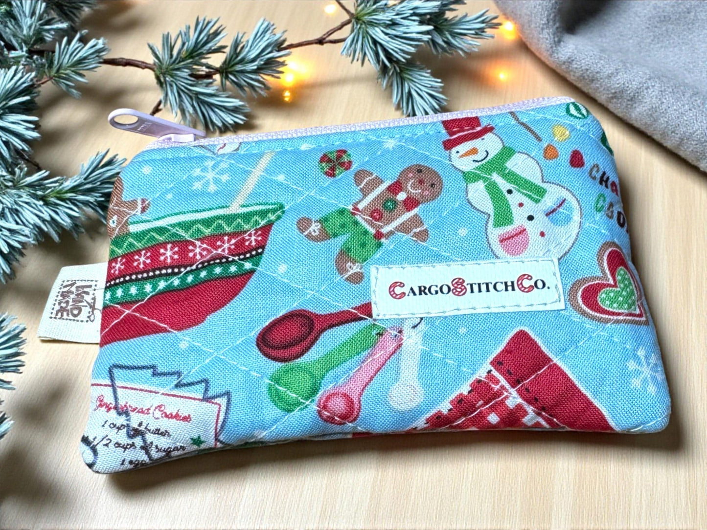 Quilted 5×3 holiday pouch with gingerbread baking scene and snowman print, light blue background, pink zipper, no pocket — Peppermint Lane Everyday series.