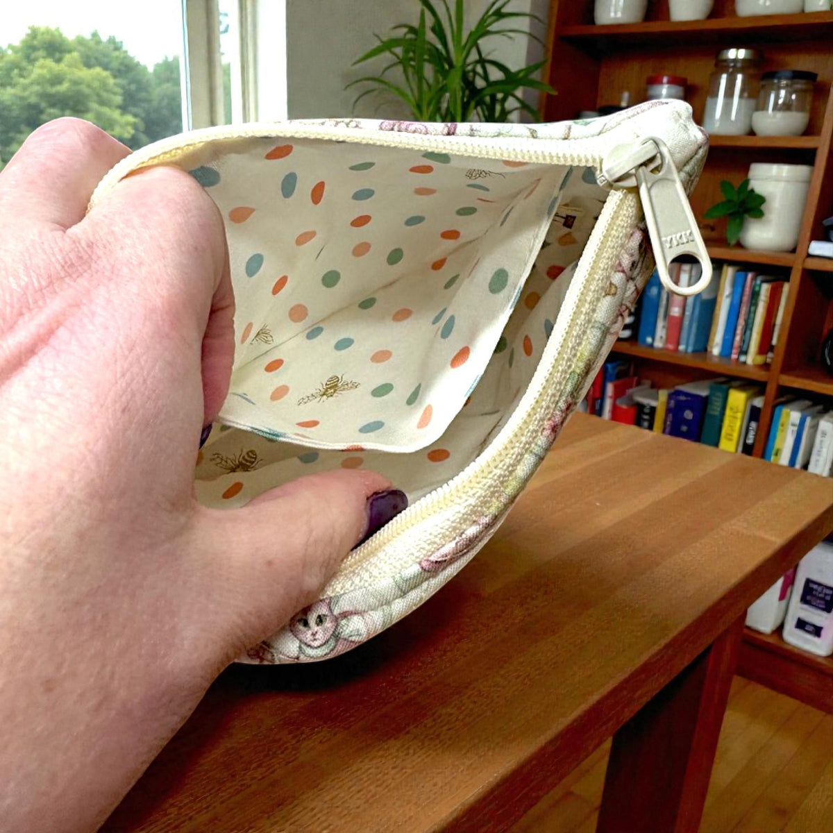 Quilted Everyday Magic zipper pouch in the Button Trail Mouse print, featuring a soft woodland scene with tiny mice, button trails, and gentle greenery, photographed on a wooden table near a window.
