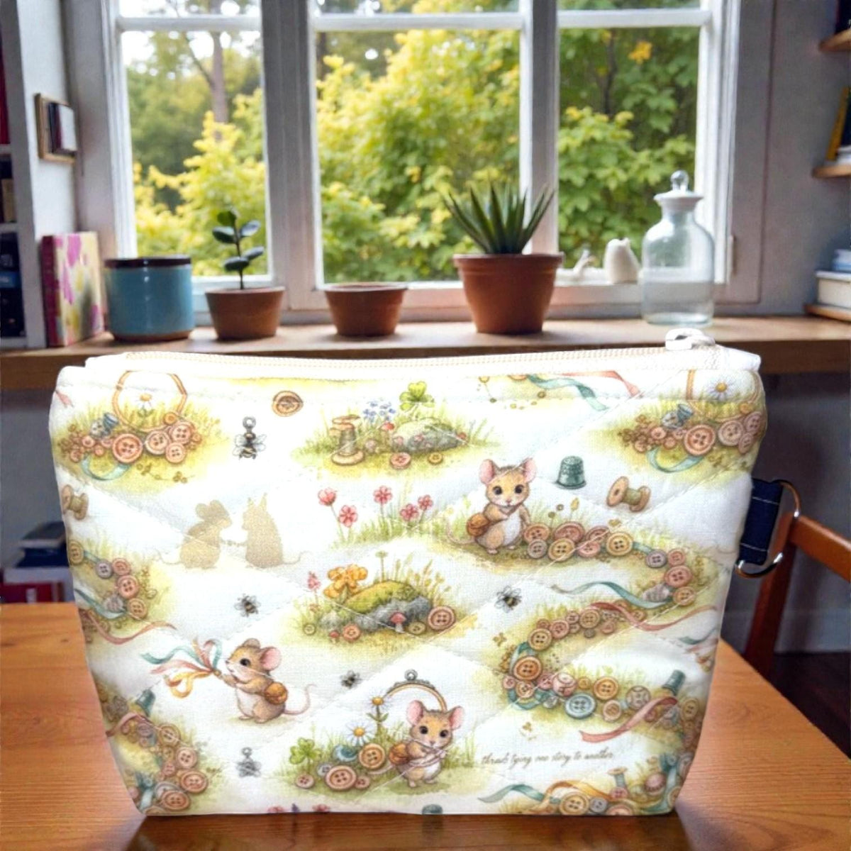 Quilted Everyday Magic zipper pouch in the Button Trail Mouse print, featuring a soft woodland scene with tiny mice, button trails, and gentle greenery, photographed on a wooden table near a window.