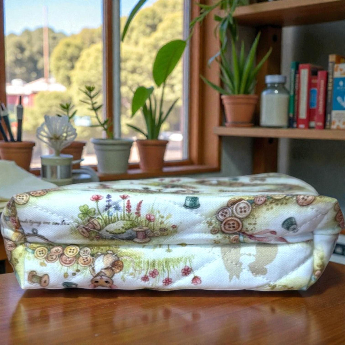 Quilted Everyday Magic zipper pouch in the Button Trail Mouse print, featuring a soft woodland scene with tiny mice, button trails, and gentle greenery, photographed on a wooden table near a window.