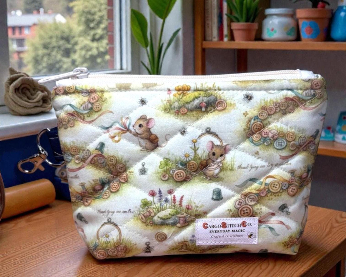 Quilted Everyday Magic zipper pouch in the Button Trail Mouse print, featuring a soft woodland scene with tiny mice, button trails, and gentle greenery, photographed on a wooden table near a window.
